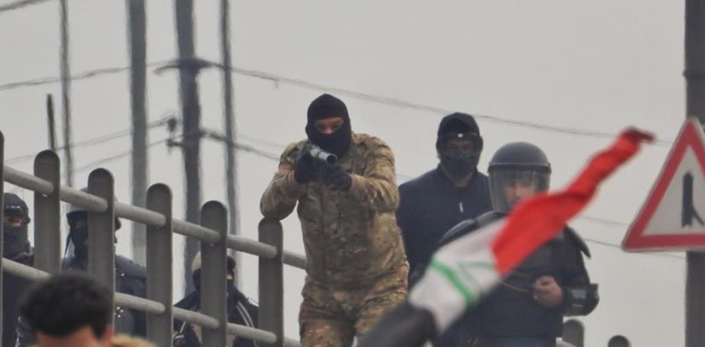 Masked Iraqi security official aims a tear gas grenade launcher at protesters